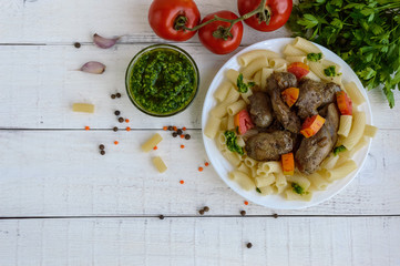 Pasta and fried goose liver (chicken, duck) with pesto and tomato on a white background. The top view