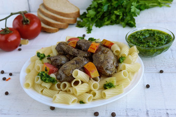 Pasta and fried goose liver (chicken, duck) with pesto and tomato on a white background.
