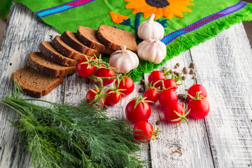 Stilllife on wooden background: tomatoes, black bread, garlic, f