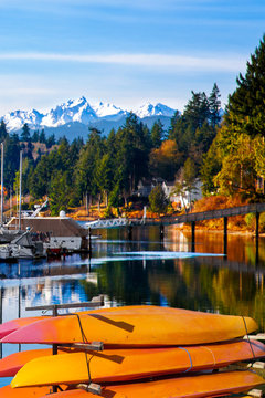 Orange kayaks stacked by the water. Snow covered mountains in the background.