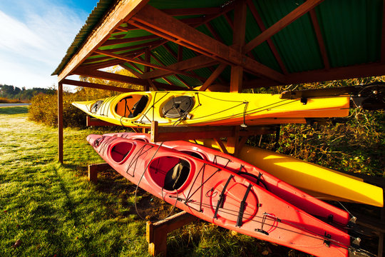 Red and yellow kayaks stored outside on a rack protected by a shelter