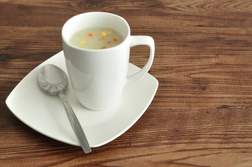A mug of vegetable soup displayed with a spoon and plate 