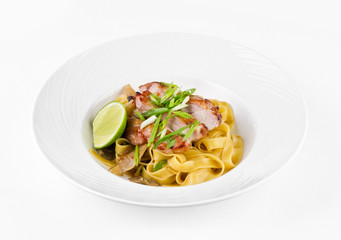 Pasta Fettuccine and caramelized pork with green onions and lime on a plate on a white background