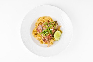 Pasta Fettuccine and caramelized pork with green onions and lime on a plate on a white background, top view