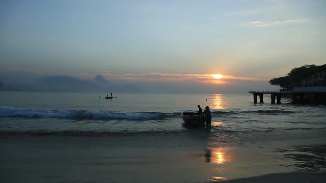 Fishermen push their boat out to sea in Brazil at sunset
