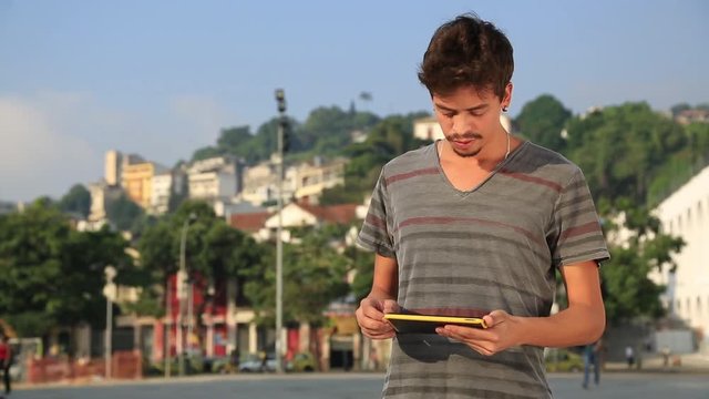 A young man standing on the street looks at his tablet