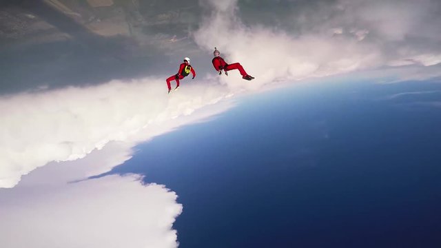Two skydivers dancing in cloudy sky. Sunny day. Extreme sport. Stunt. Contest. Professionals