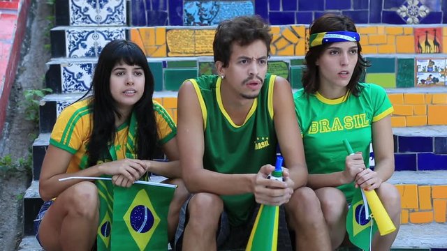 Three Brazilian football fans sit outside and cheer for their team