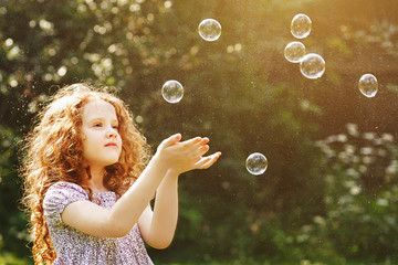 Curly little girl catch a soap bubbles.