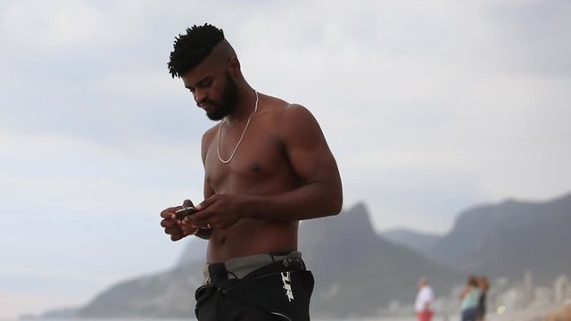 A young man stands on the beach and texts on his smart phone