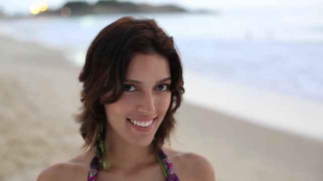 A young woman smiles at the camera as she stands on the beach