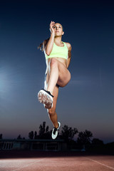 Fototapeta na wymiar Fit young woman running on track field at night.
