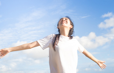 Happy relaxed asian woman breathing deep fresh air and raising arms on the beach with blue sky background