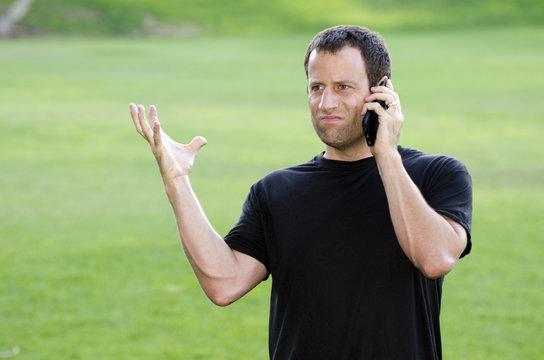 Frustrated angry man on his cell phone outdoors in a black t-shirt.