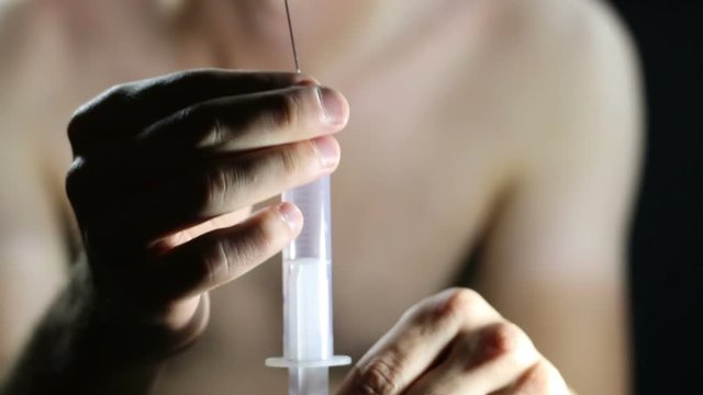 Unclothed junkie prepares a syringe for injection