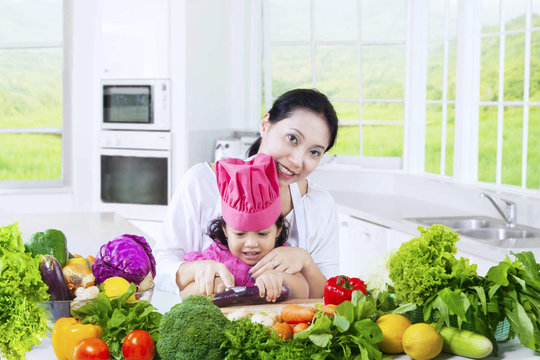 Adorable girl and mother cooking vegetables