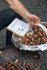 Vendor in Rome offering roasted chestnuts to tourists. Sign reads: "Brown cooked on the grill."