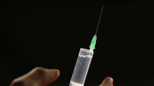 Man flicks syringe prior to drug injection, to collect and release the air out of the syringe.