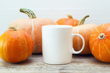 White coffee mug with small pumpkins on a wooden table.