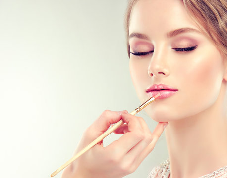 Fototapeta Hand of make-up master, painting lips of young beautiful model. Makeup in progress.