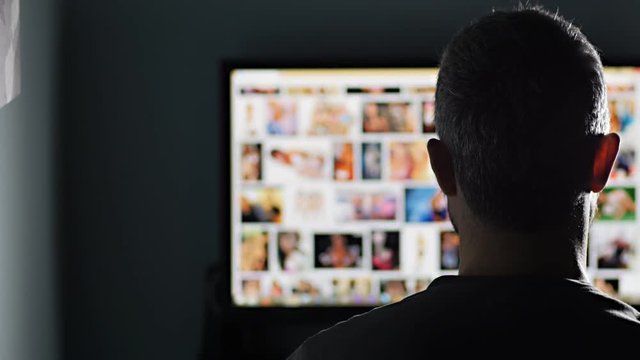 man watches surfing pornography site looking for virtual sex at night in a dark room,screen is out of focus uhd 4k,useful to represent internet easy porn accessibility and social issue