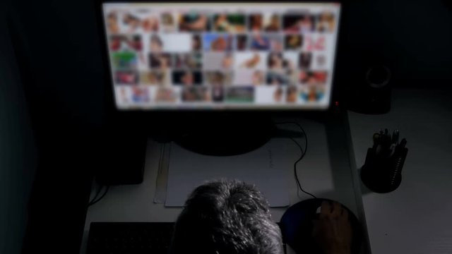 man watches surfing pornography site on pc looking for virtual sex at night in a dark room,screen is out of focus uhd 4k,useful to represent internet easy porn accessibility and social issue