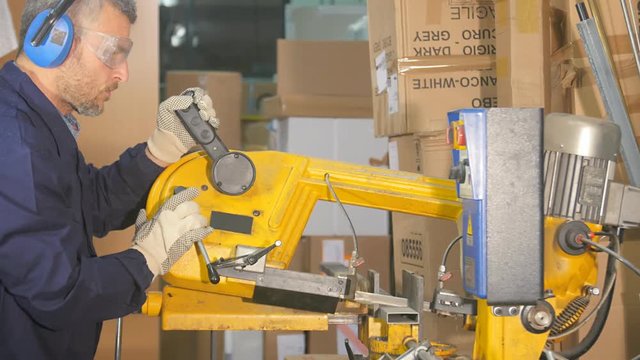workman sawing metal steel bar in a  workshop with industrial circular saw