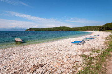 Obraz premium Sun beds on pebbly beach with crystal clear water. Corfu, Greece.