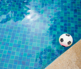 Fototapeta na wymiar A plastic football floating in the blue water of a swimming pool