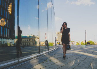 beautiful girl in a black dress goes in the background of the business center and talking on the phone