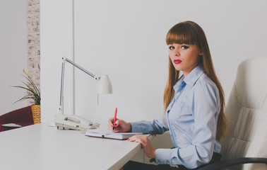 the girl Secretary making notes in the diary at the Desk in the office