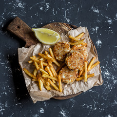 Fish balls and potato chips on rustic cutting board on a dark background. Top view
