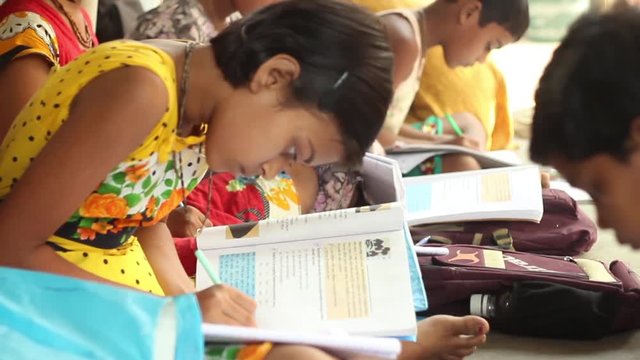 Boy and girl students diligently study in a village school in Bengal, India. Tilt shot from the side, narrow depth of field