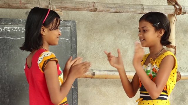 Two girl students play a clapping game in a village school in Bengal, India. No sound