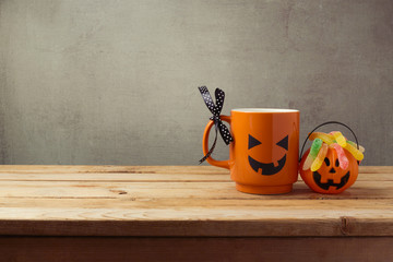 Coffee cup as jack o lantern pumpkin and candy for trick or treat on wooden table. Halloween concept