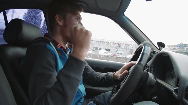 Young happy man driving a car dancing. Inside shot