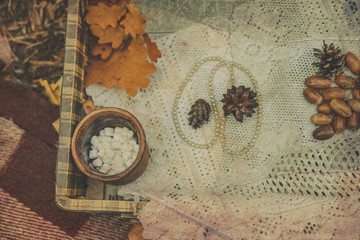 White perls with  autumnal acorns and cones,yellow leaves,cup with candy on the lace tablecloth.Vintage toned background.Selective Focus