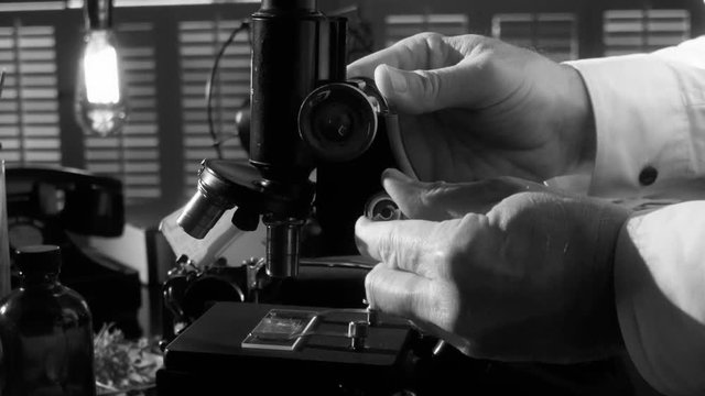 A botanist or biologist working with an old microscope with other items in the scene that indicate the era is circa 1940.