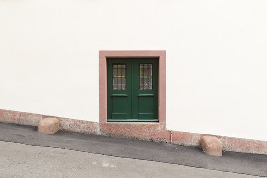 Eine weisse Wand mit einer kleinen grünen Tür und einem pinkfarbenen Rahmen in der Mitte des Bildes.