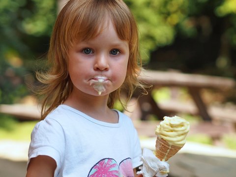 Little blond girl eating ice cream. She is dirty and the ice cream is melting. Summer time outdoor.