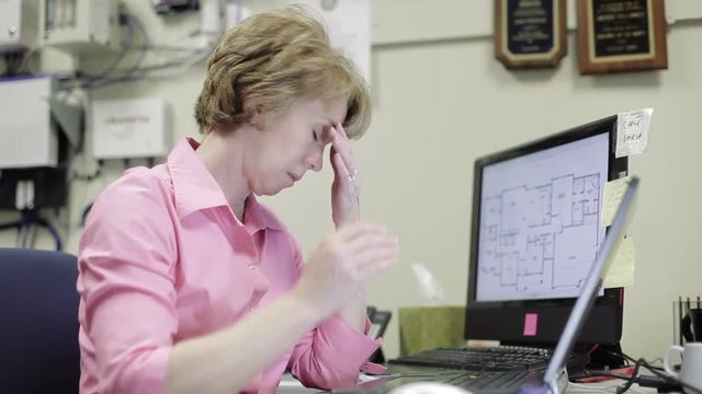 Mature female telecommunications or network admin with a stress headache working in her office.
