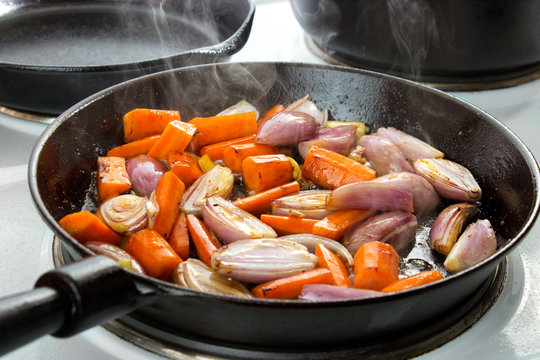 Frying vegetables (carrots , onions , shallots and garlic) in cast iron skillet on electronic stove stop