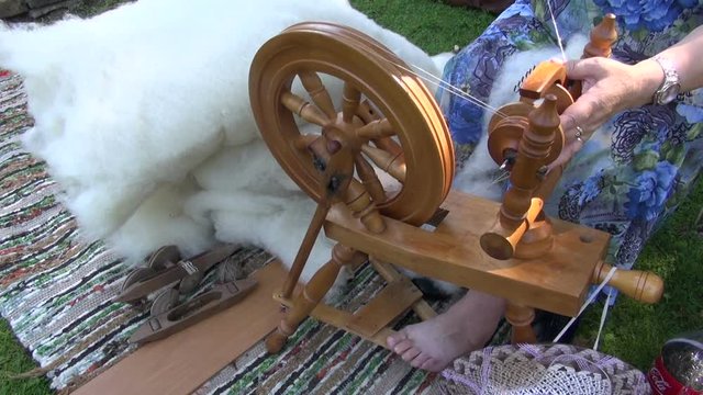 Respectable age woman using spinning wheel  to spin wool outdoors during medieval fair