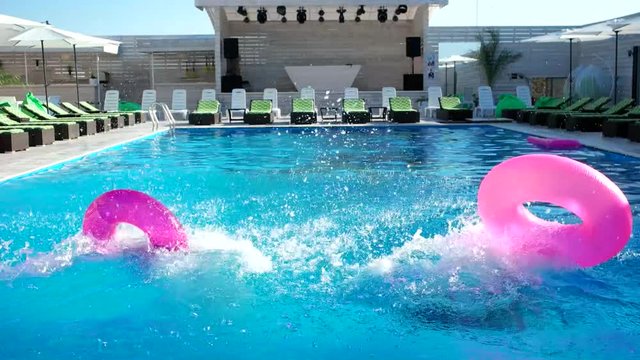 jump into the water, friends into the pool.girls with sexy figure on holiday. Excited young friends jumping into swimming pool on a summers day fun summer vacation rubber ring for swimming in the hand