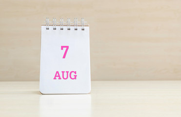 Closeup surface note book with pink 7 aug word  in page on blurred brown wood desk and wood wall textured background with copy space under window light
