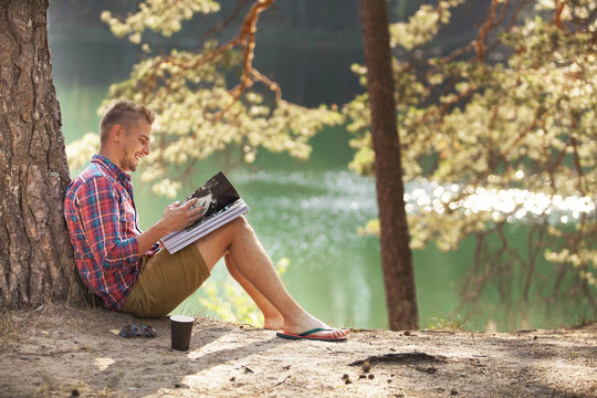 Young Man reading magazine outdoor with lake on background Summer vacations and Lifestyle concept