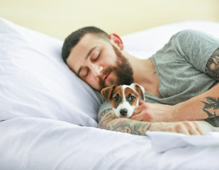 Handsome man with cute dog sleeping in bed