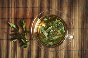 Cup of sage tea on wicker mat background