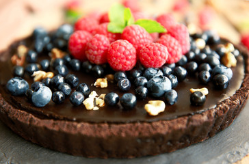 Delicious chocolate tart with berries and nuts on slate plate, closeup