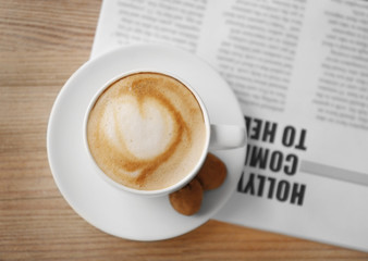 Cup of fresh coffee and morning newspaper on wooden table